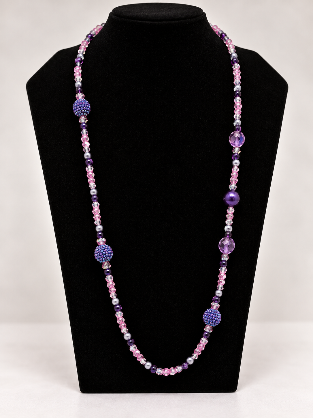 Pink and purple crystal beaded statement necklace on black jewelry display