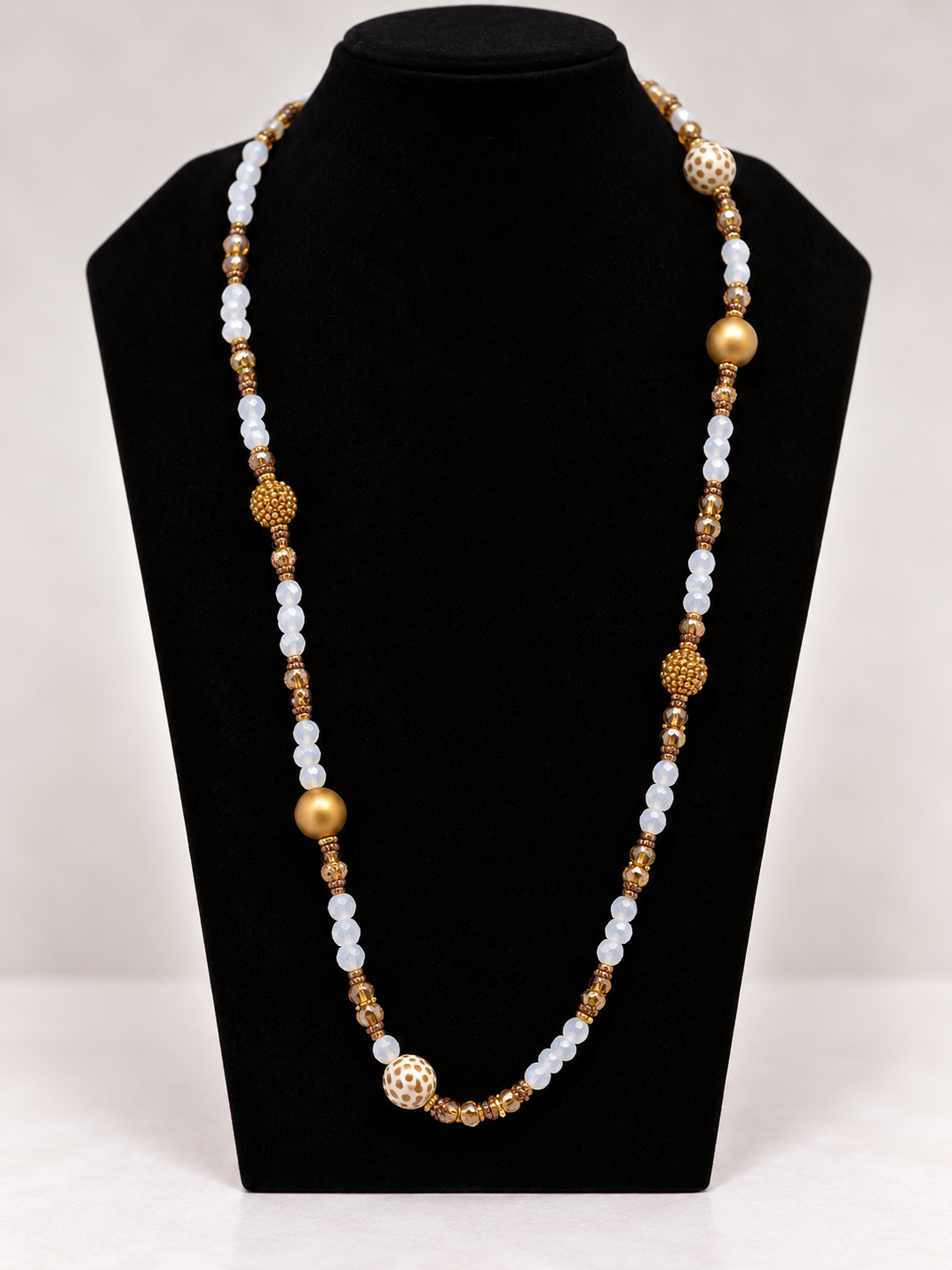 White and gold beaded statement necklace on black jewelry display