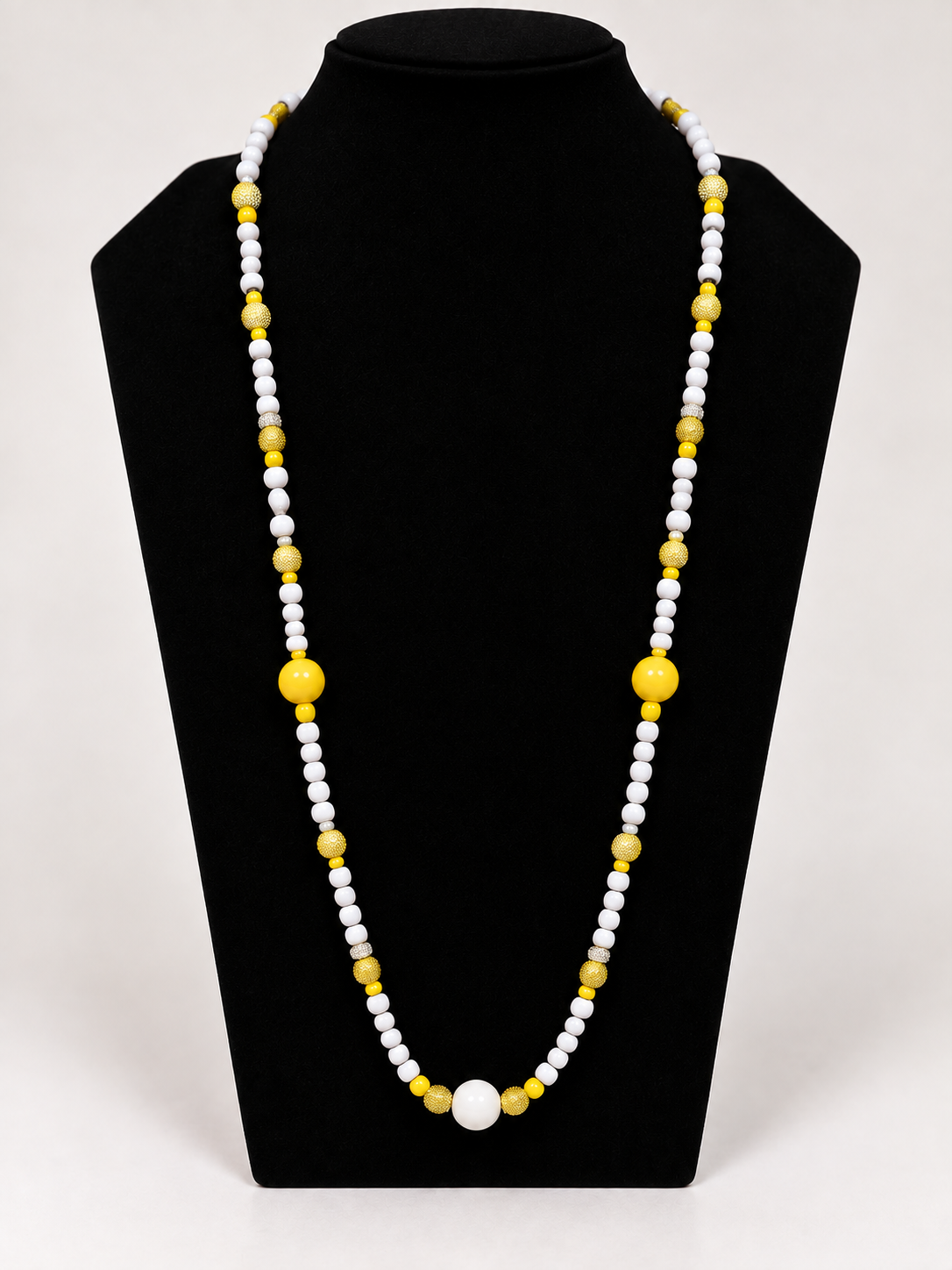 White and yellow beaded statement necklace on black jewelry display